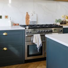 Kitchen with blue cabinetry, white countertop, and marble blacksplash. A silver range oven and hob has a tea towel hanging off the handle