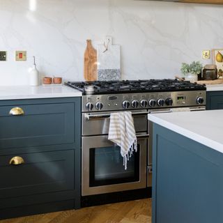 Kitchen with blue cabinetry, white countertop, and marble blacksplash. A silver range oven and hob has a tea towel hanging off the handle