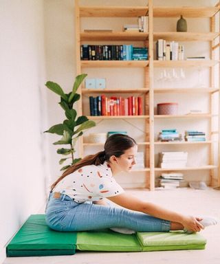 A female sat on a green gym floor mat with shelving behind