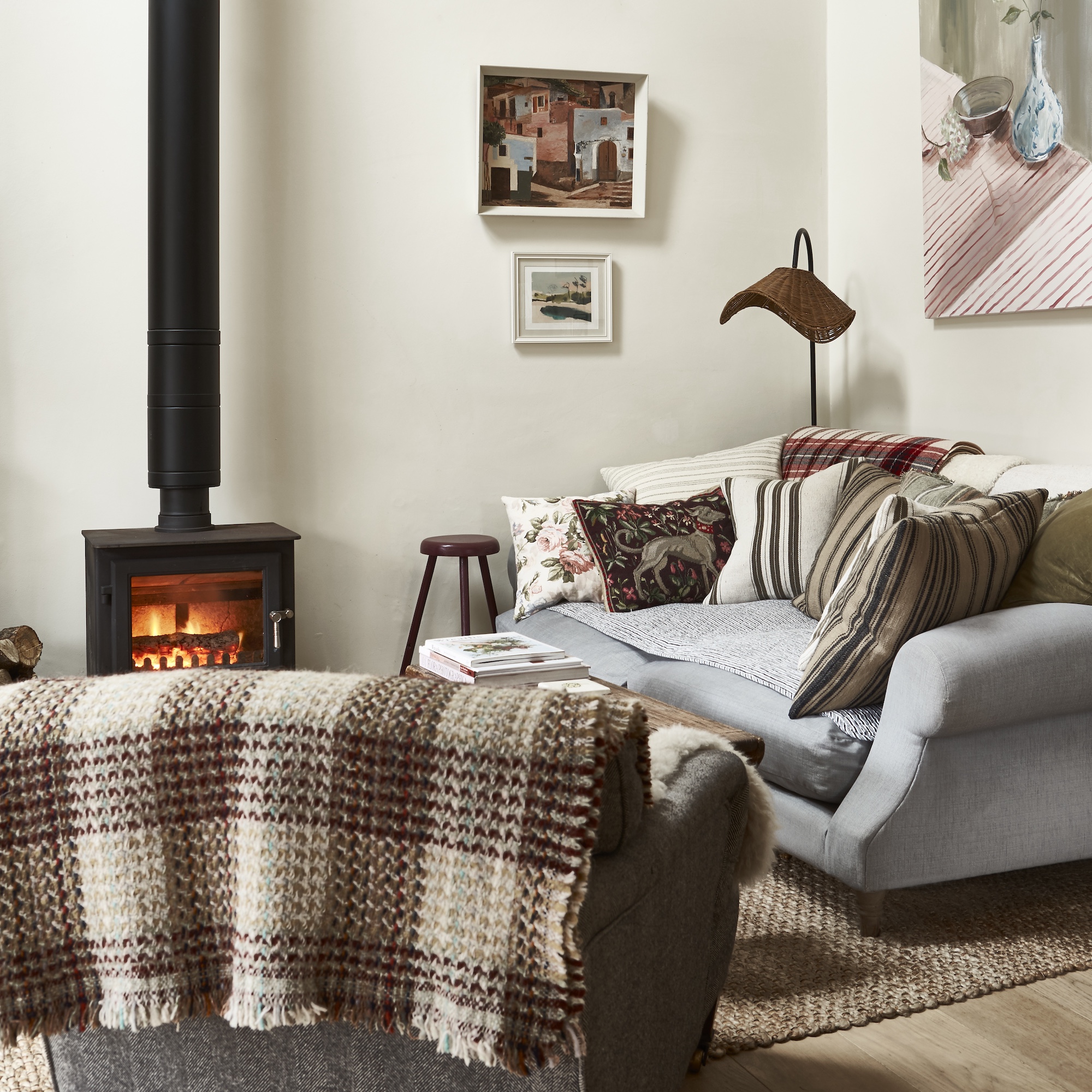 cream painted living room with black wood burner with tall chimney, grey sofa and armchair with checked throw