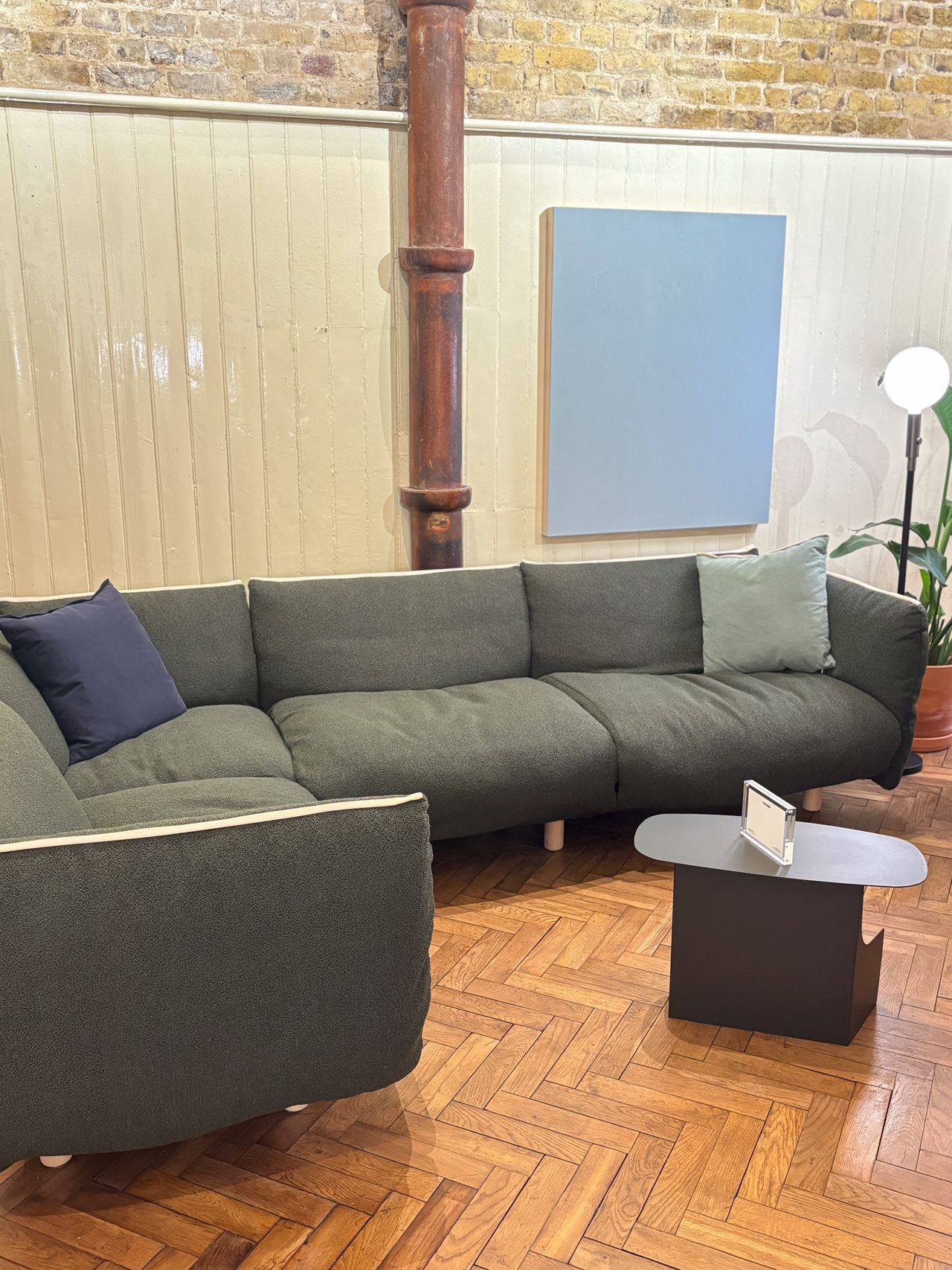 a green cozmo pillow sofa in a showroom with parquet floors and panelled wall