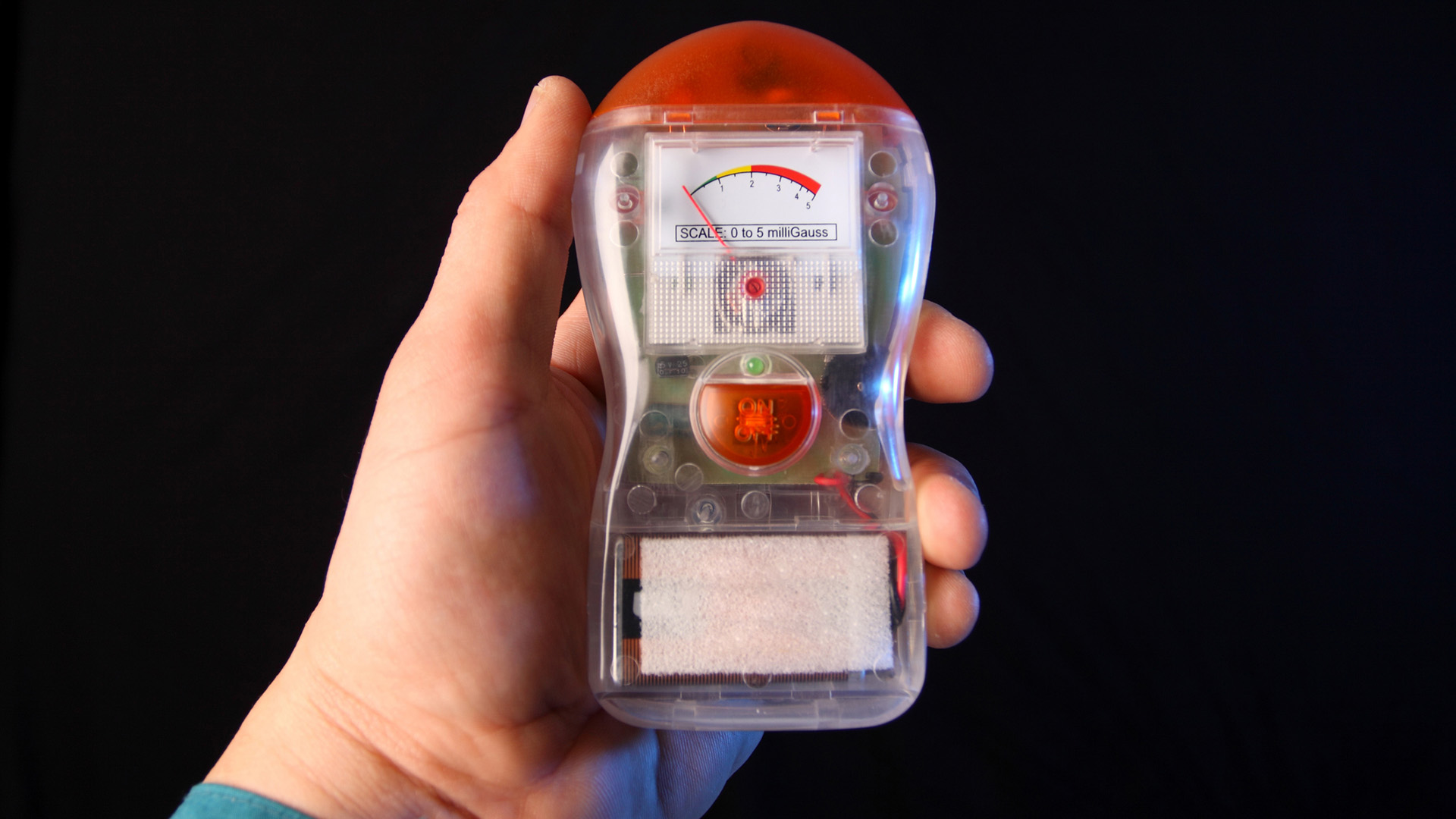 A person holds a small device in their hand against a black background