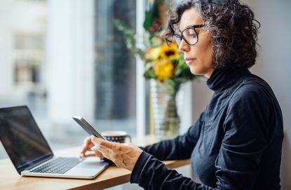 Woman working at laptop and using her phone.