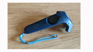 Image shows an HTC Vive Pro 2 controller on wooden furniture.
