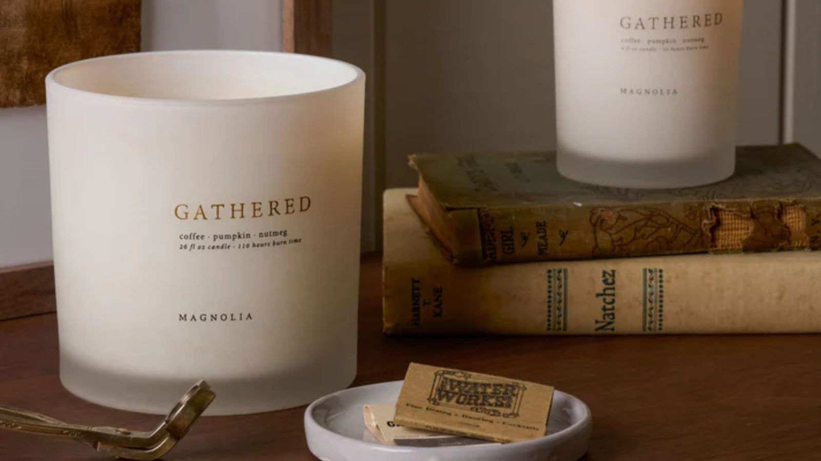 White &#039;Gathered&#039; candles on top of a wooden table and a stack of leather-bound books