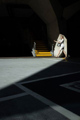 Photograph of a woman walking in a shaft of sunlight. Photographed by Sean Tucker