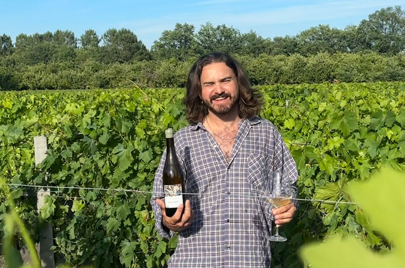 Tom Heading in a Graves vineyard in Bordeaux, holding a bottle and a glass of wine.