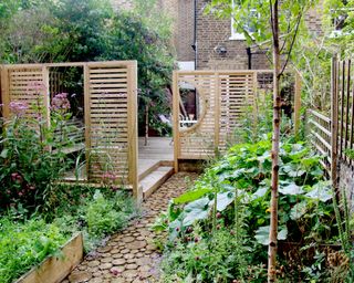 timber screens used to zone a small garden with a decking, raised beds and a log style pathway
