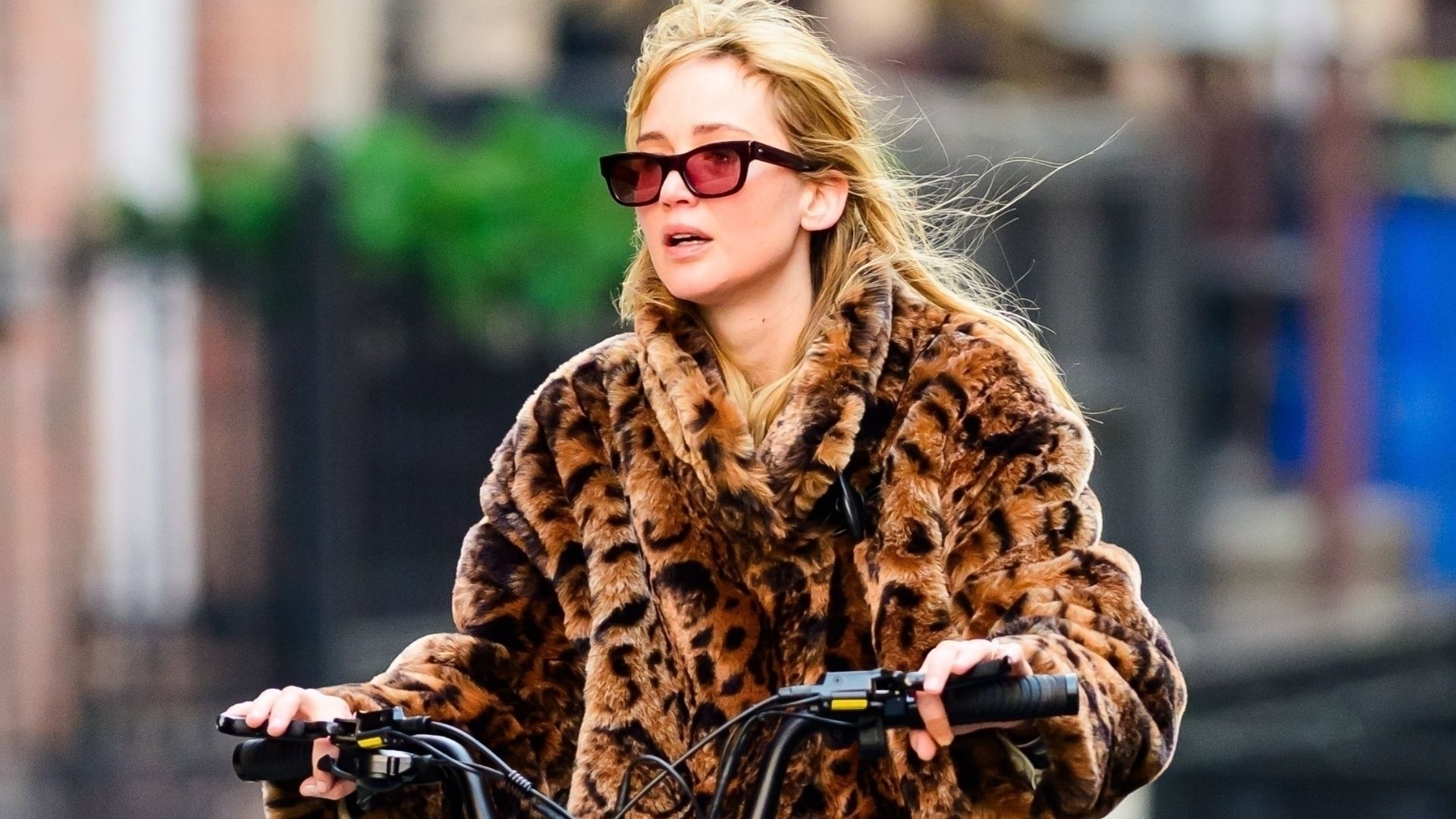 Jennifer Lawrence cycles down the street in New York wearing blue jeans with rounded-toe boots and a leopard print jacket
