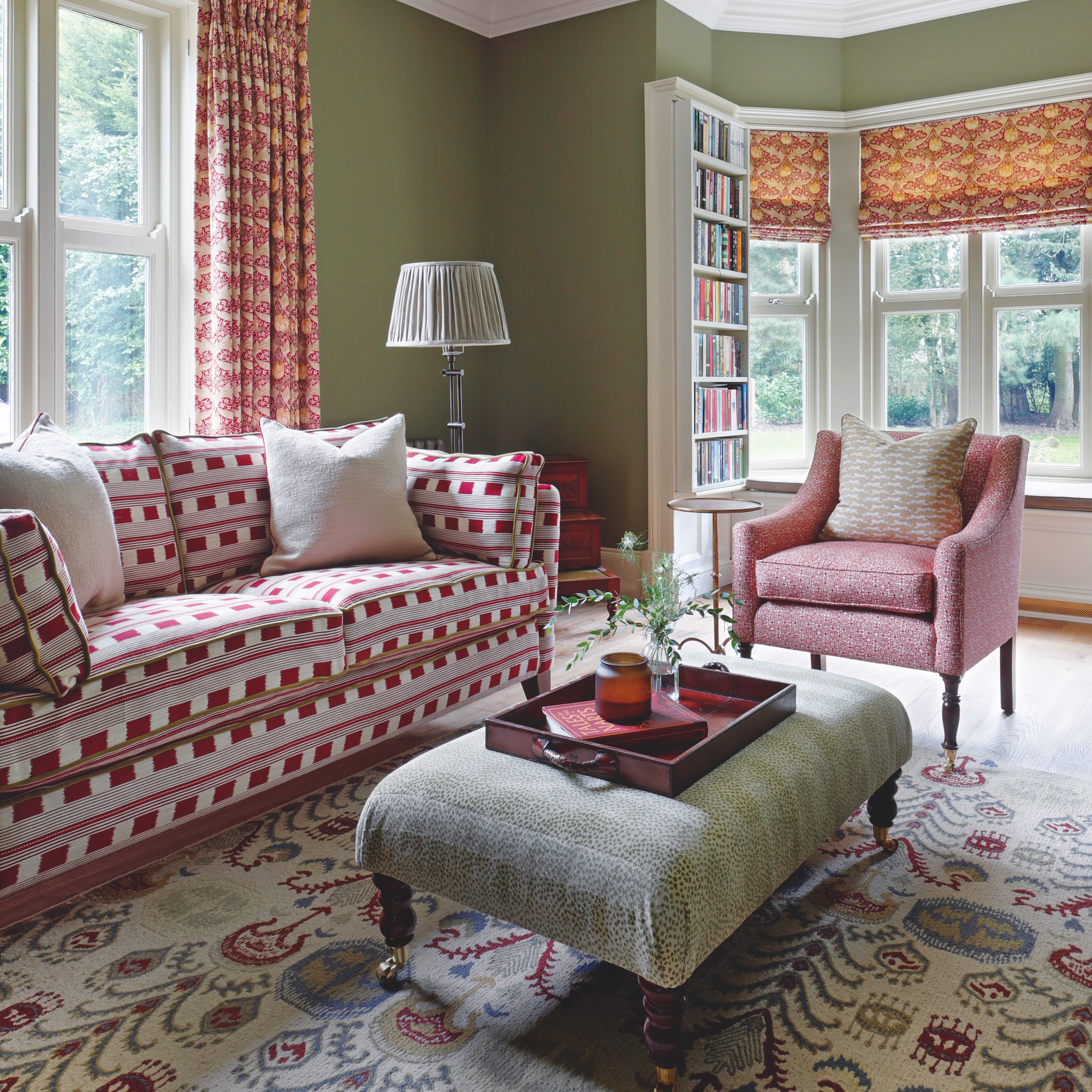 sitting room with sage green walls and sofa in deep pink ikat fabric, with pink upholstered armchair and green fabric covered ottoman