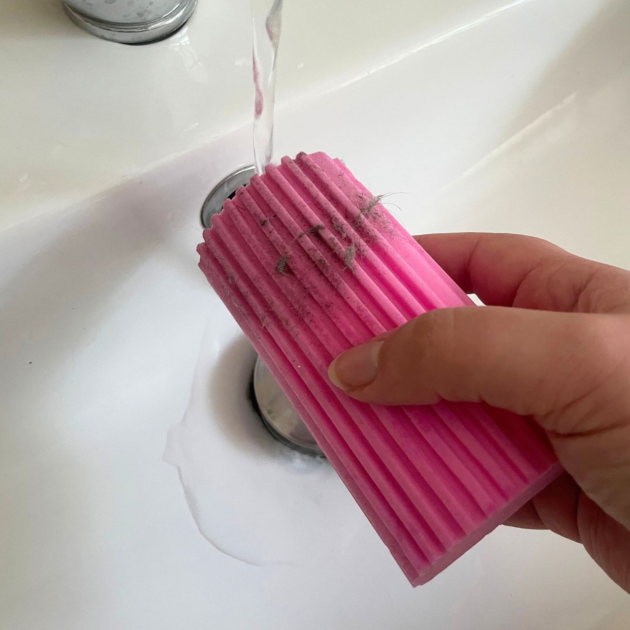Cleaning a pink Damp Duster covered in dust under running water
