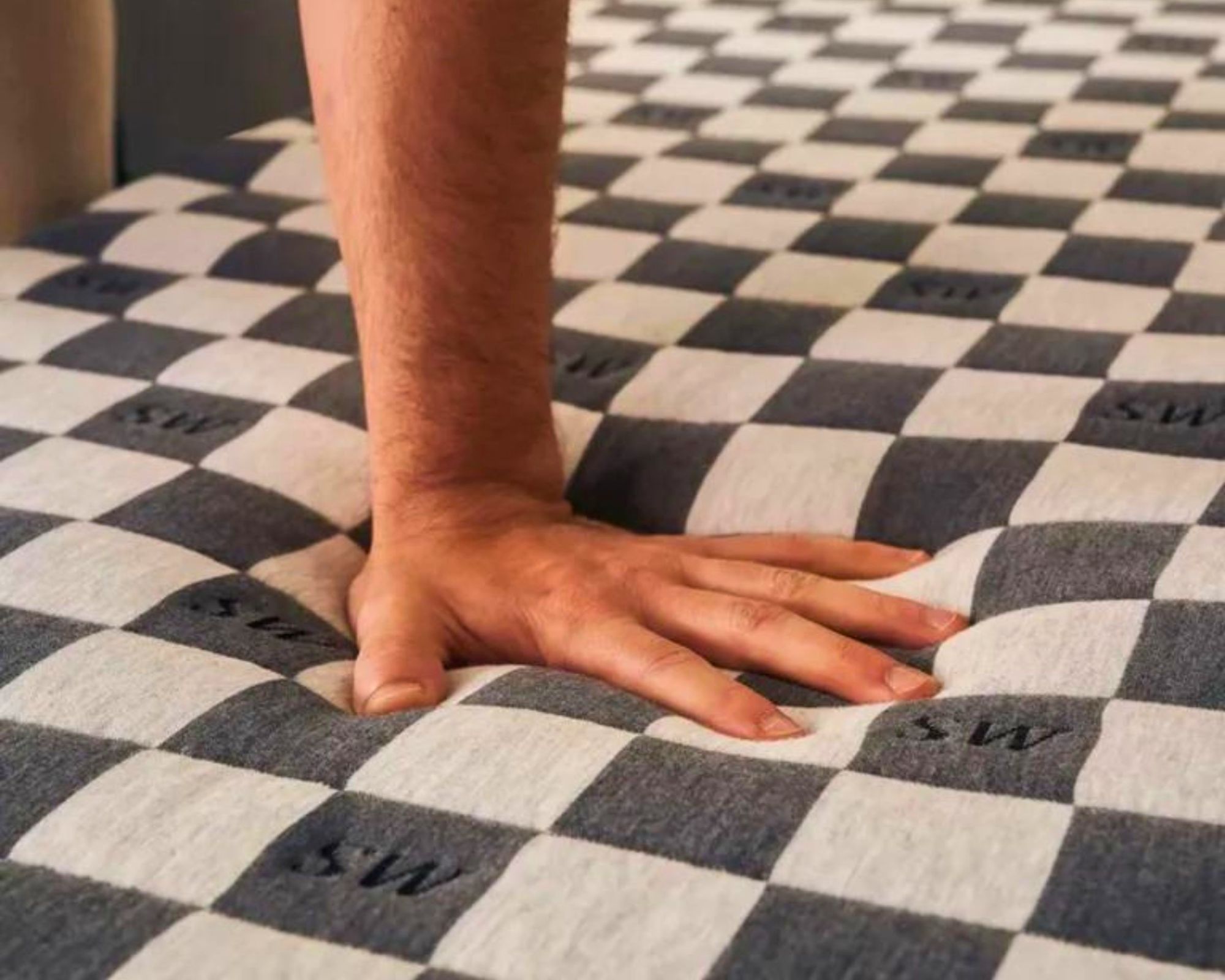 A man's arm and hand pressing into the chequered black and white SweetNight Prime Memory Foam Mattress.