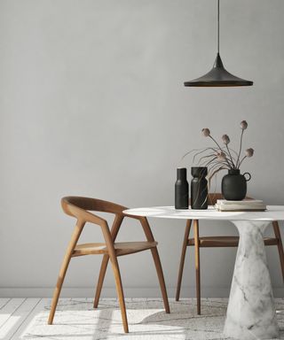 Large matt black pendant light above white marble table and wooden chairs