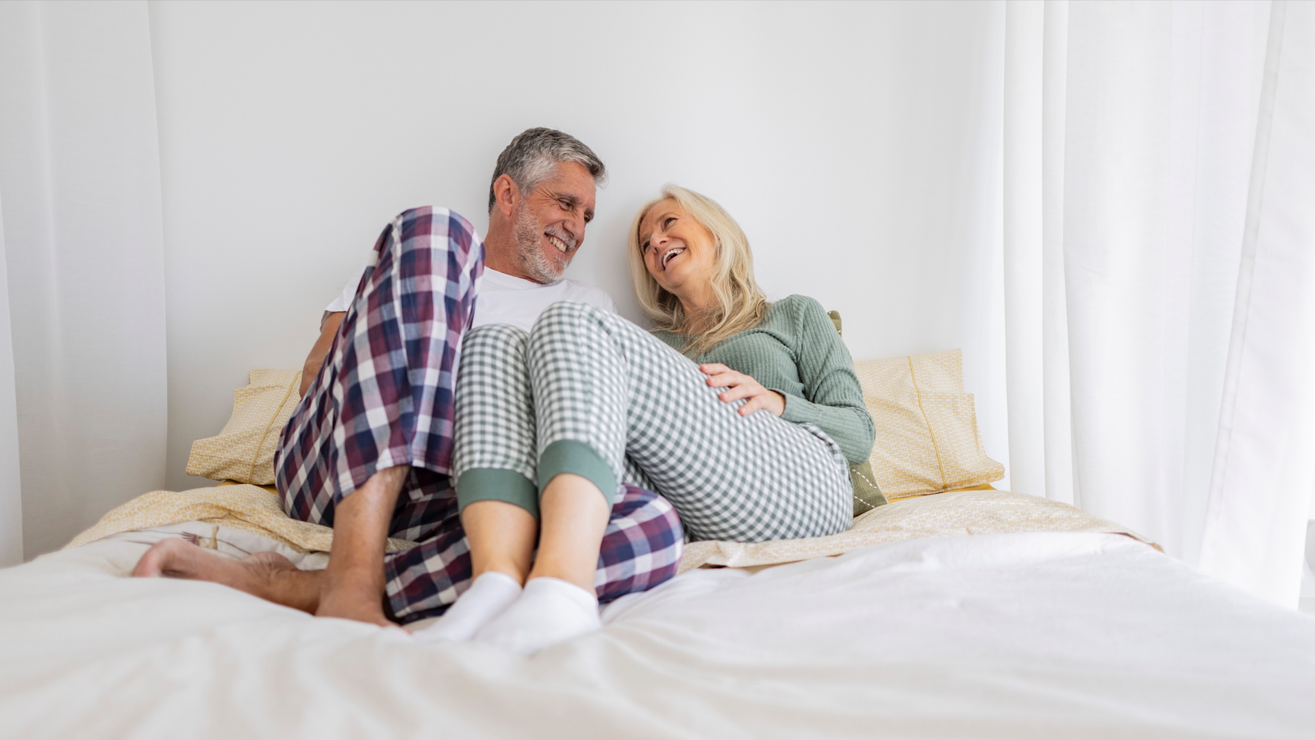 A couple in their 50s laughing and cuddling in bed