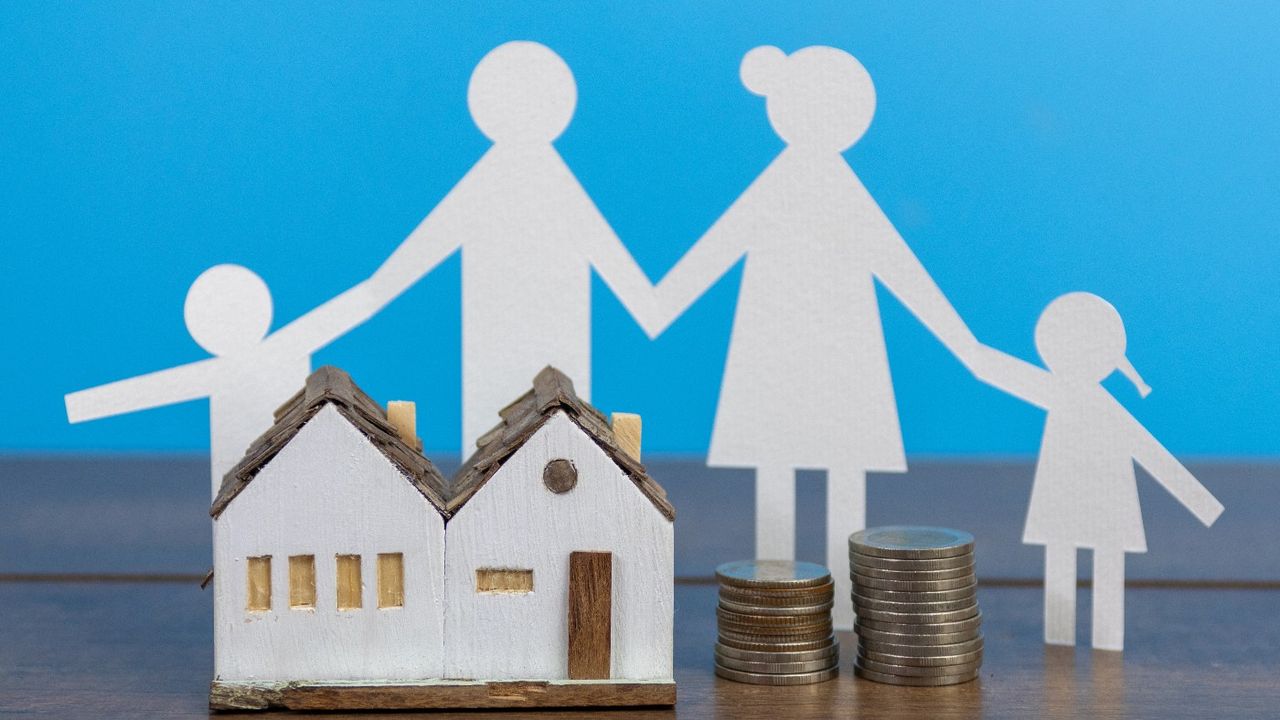 Paper cut out of family next to house and pile of coins