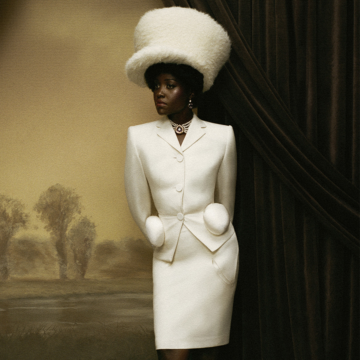 lupita wears a white hat, white blazer, and white pencil skirt.