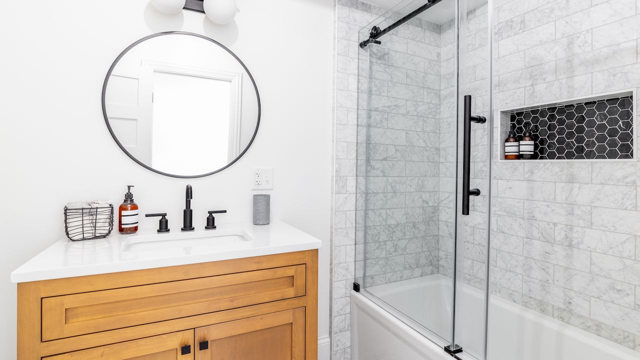 A beautiful bathroom with a wood vanity, custom tile shower and floor, and a sliding glass door with black hardware.