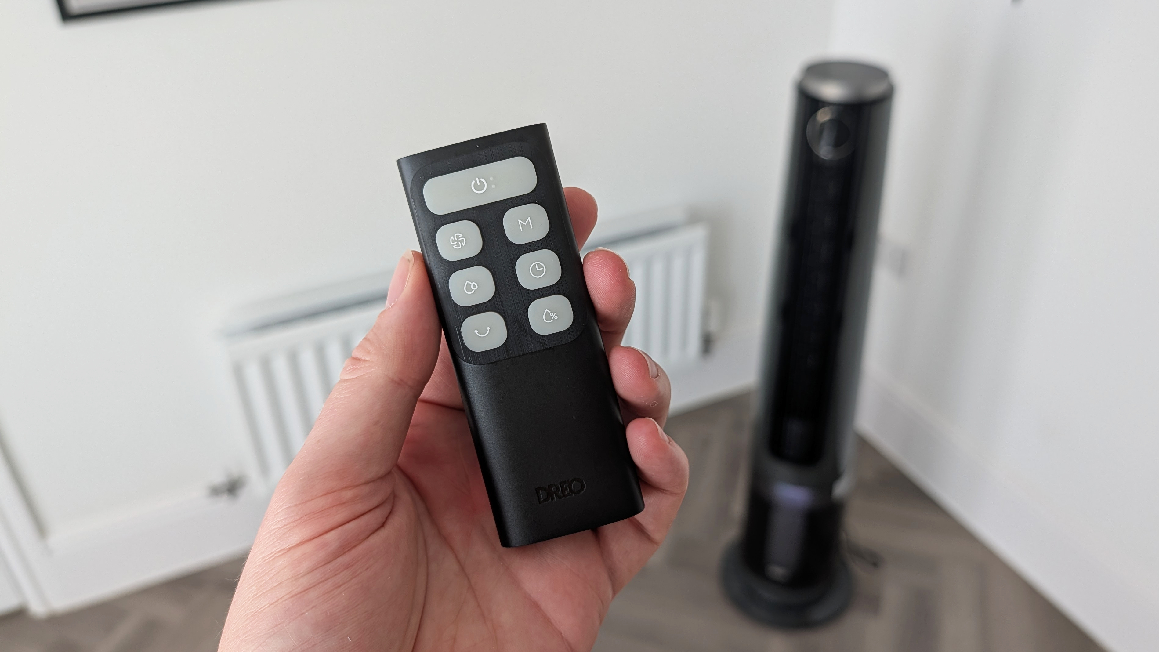 A man's hand holding the remote for the Dreo Smart Misting Fan 765S.
