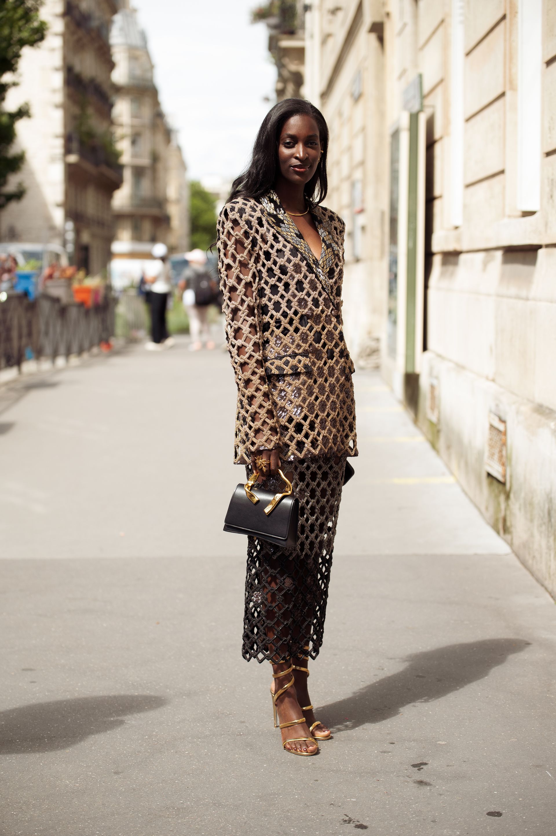A Couture Fashion Week attendee wears an embellished blazer and skirt with gold heeled sandals