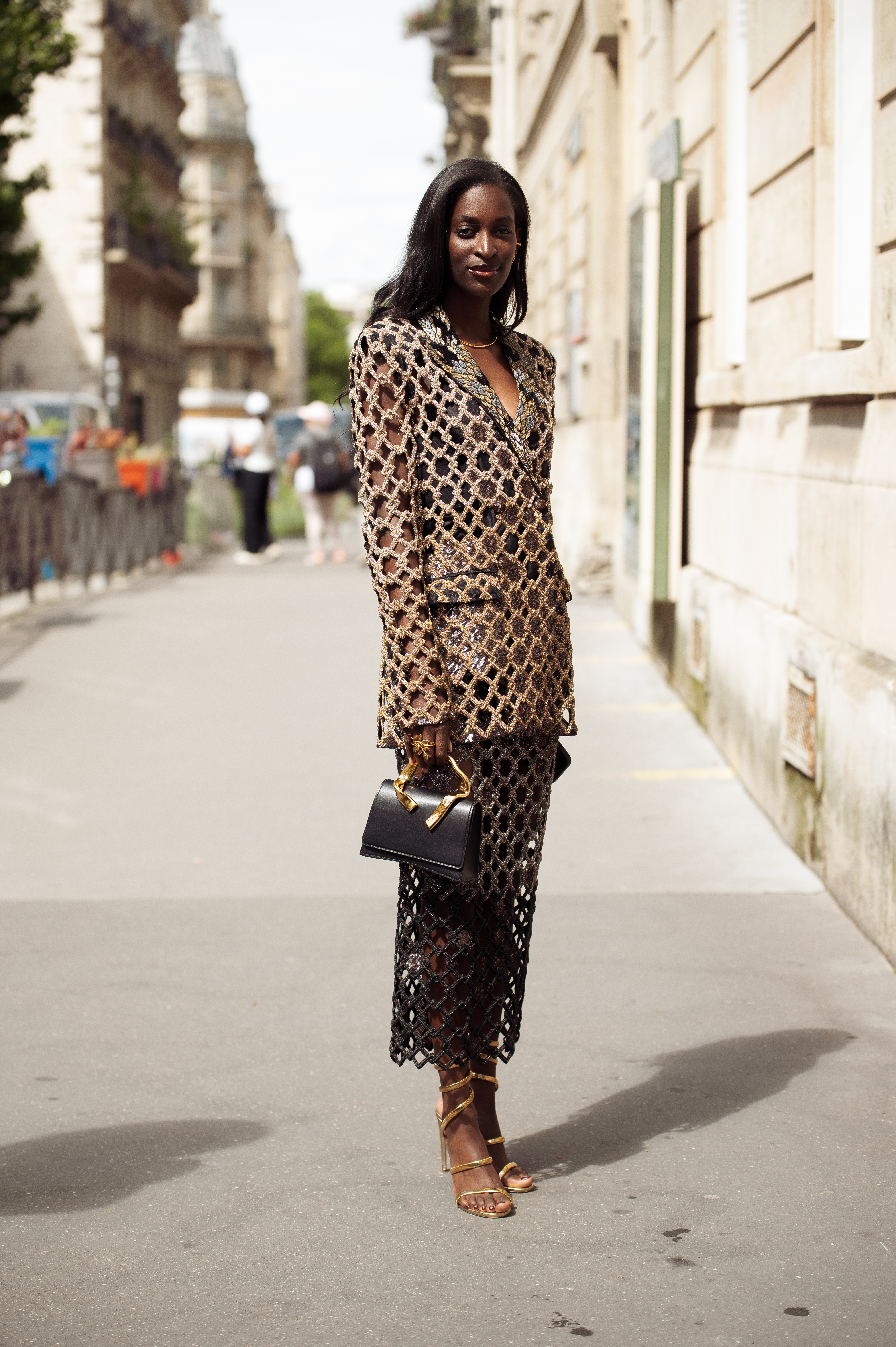 A Couture Fashion Week attendee wears an embellished blazer and skirt with gold heeled sandals