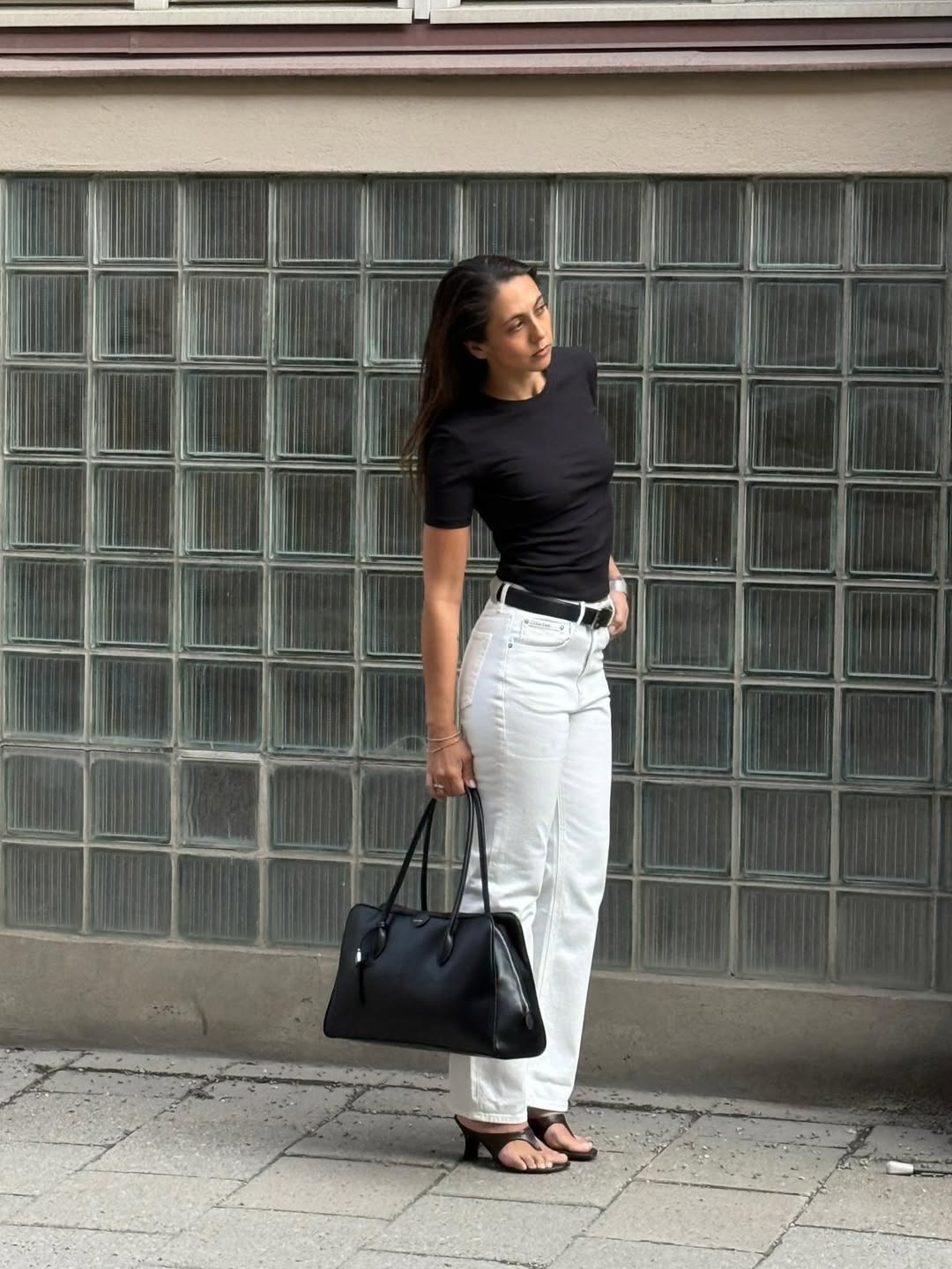 Woman wearing a black tee with white trousers and heeled thong sandals.