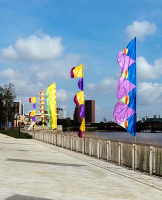 Colourful flags by the river Thames, created by Yinka Ilori for Greenwich Peninsula