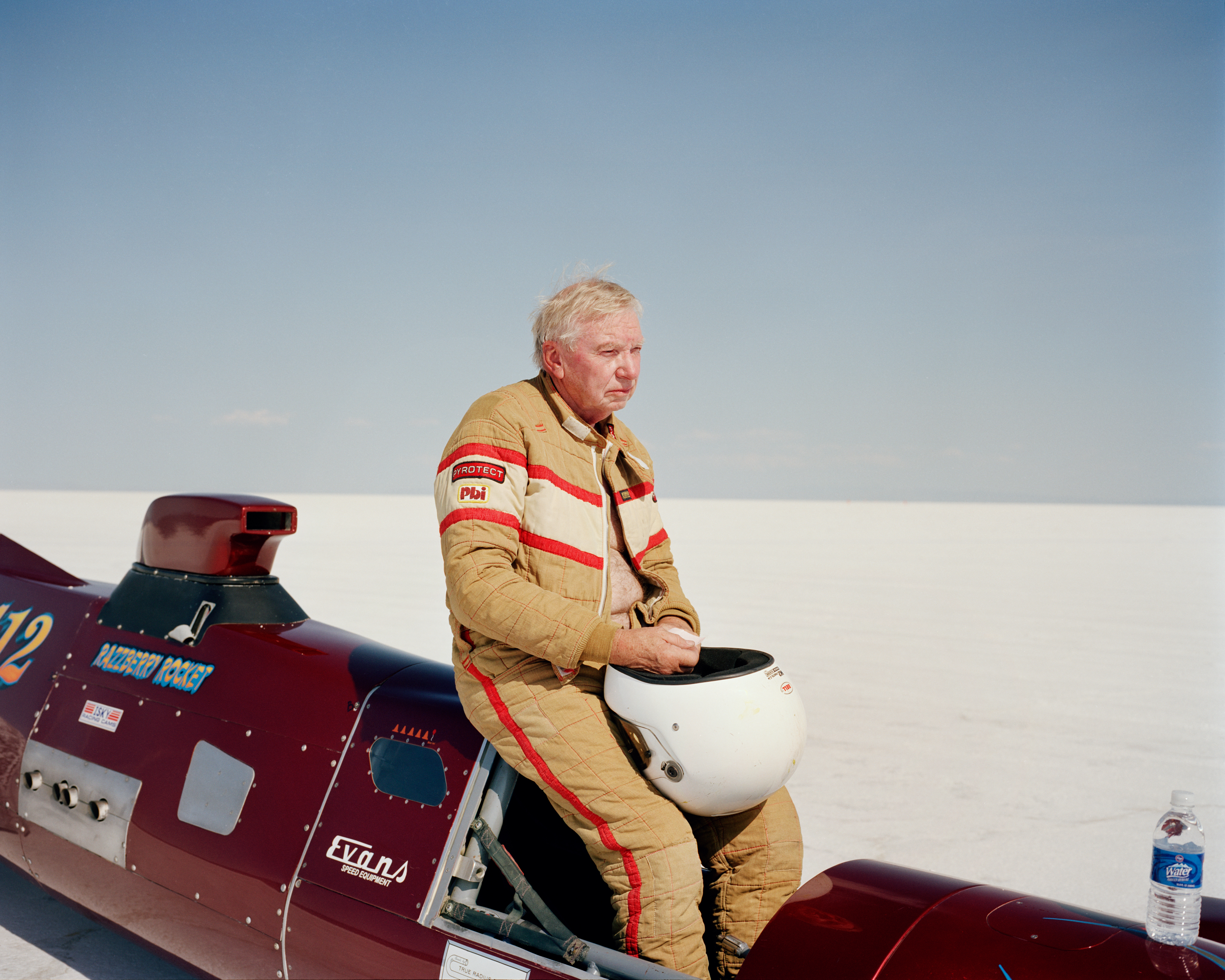 photography of man holding helmet, sitting on speed-test car
