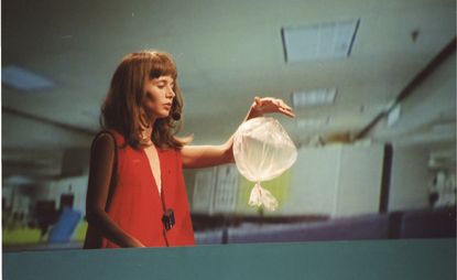 Photograph of woman holding balloon-like bag, a still from the exhibition ‘Miranda July: New Society’ at Fondazione Prada, Milan