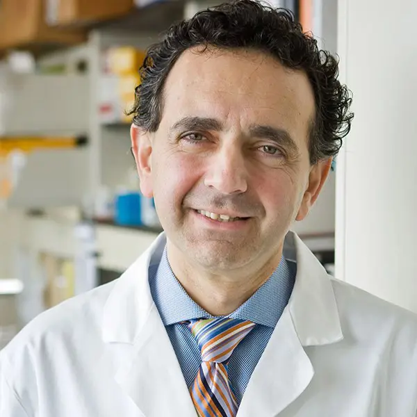 A man with short dark hair wearing a white lab coat smiles for the camera