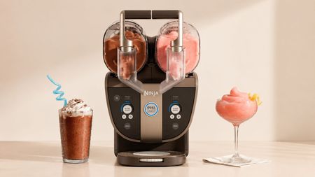 A black Ninja SLUSHi twist machine, with two dispensers, one filled with cola slush, the other with a pink slush. A glass of each on either side. 