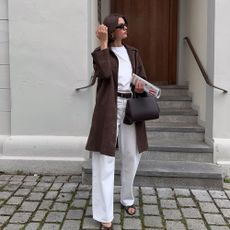 Influencer @maryljean wears white jeans with brown heels, a white-shirt and a brown knee-length jacket.