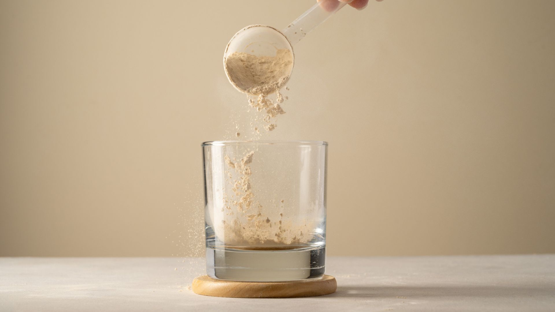 Protein powder in scoop being poured into empty glass