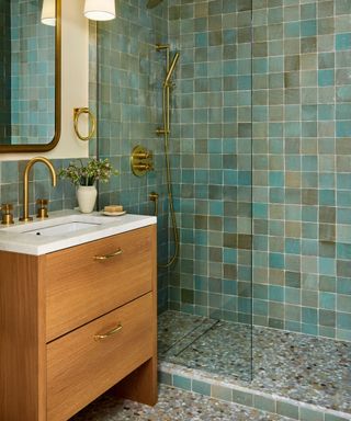 green tiled shower with terrazzo bathroom flooring and wooden vanity