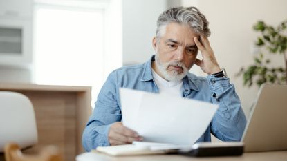 An older man looks at paperwork with a concerned look on his face.