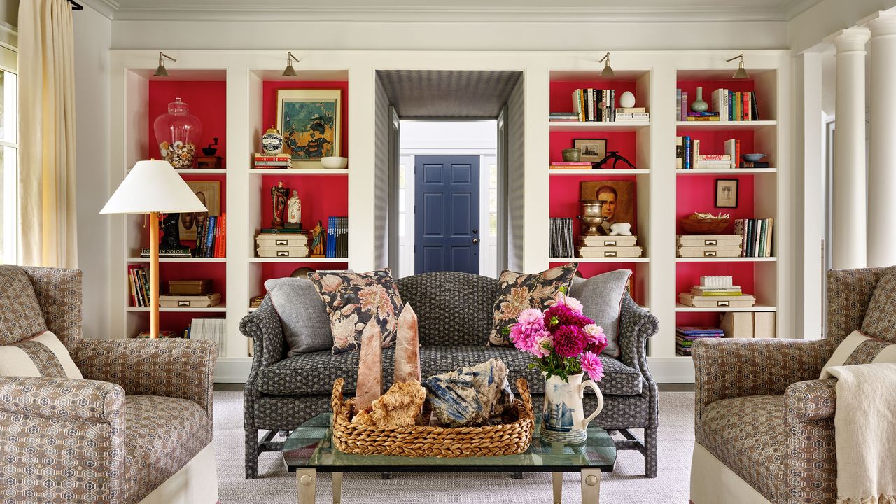 Traditional lounge with paisley upholstered 3-seater couch and open shelving in the distance filled with fuchsia