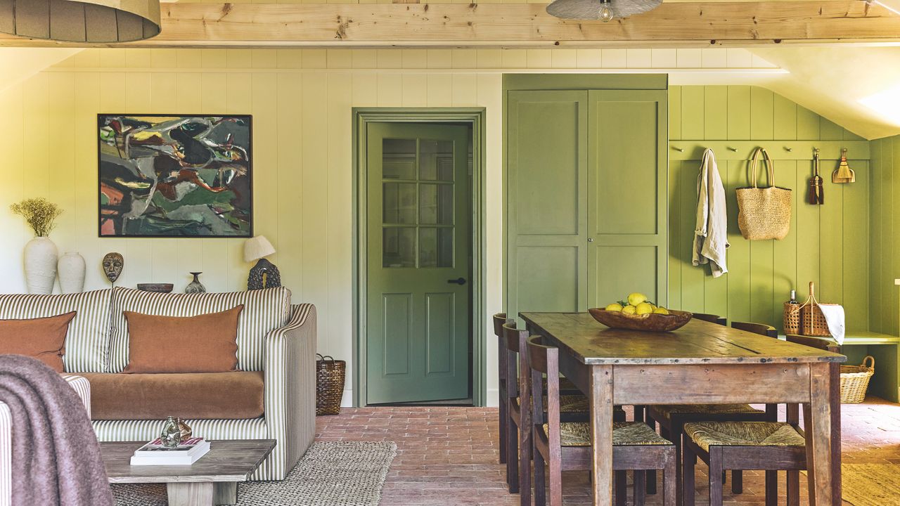 kitchen living space in converted barn with farmhouse table, striped sofa and green wood panelling