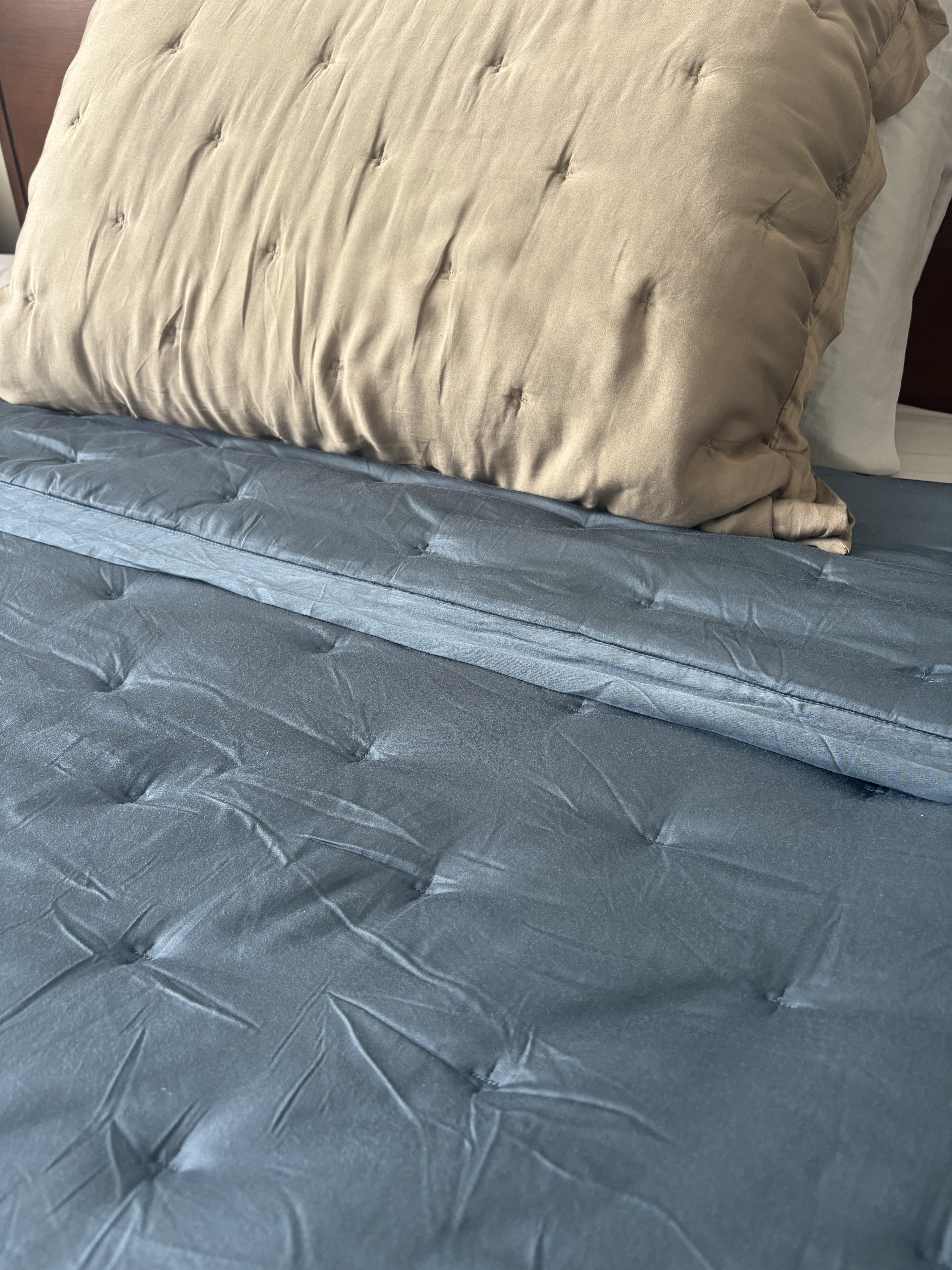 A look at a bed with a blue bamboo quilt and a beige bamboo sham.