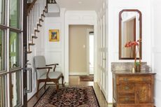 entryway with patterned rug, hard wood floors and decorated with a wooden unit, upholstered chair and large mirror.