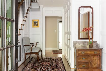 entryway with patterned rug, hard wood floors and decorated with a wooden unit, upholstered chair and large mirror.