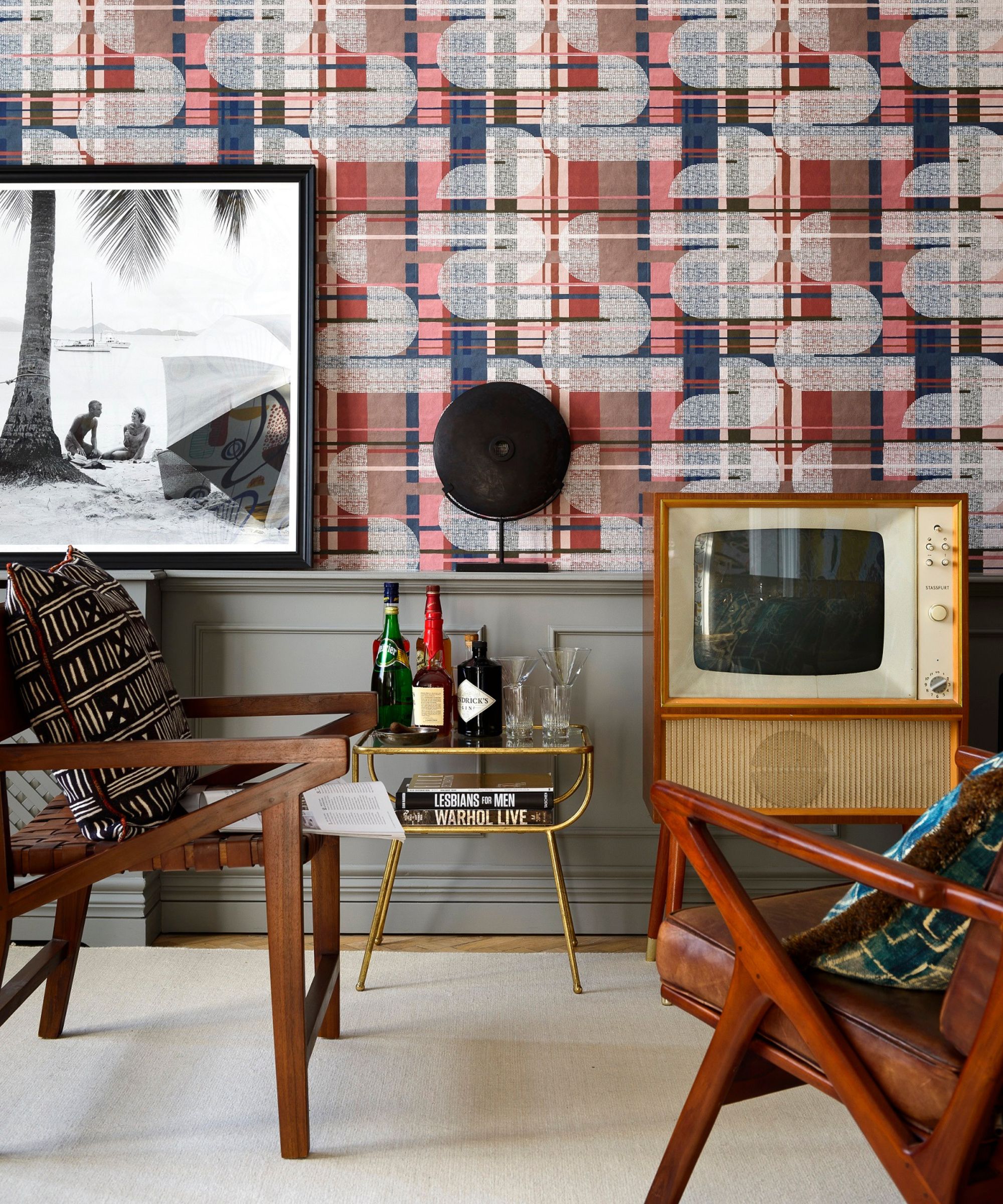 Patterned wallpaper, wooden armchairs with patterned cushions, vintage television, brass drinks trolley.
