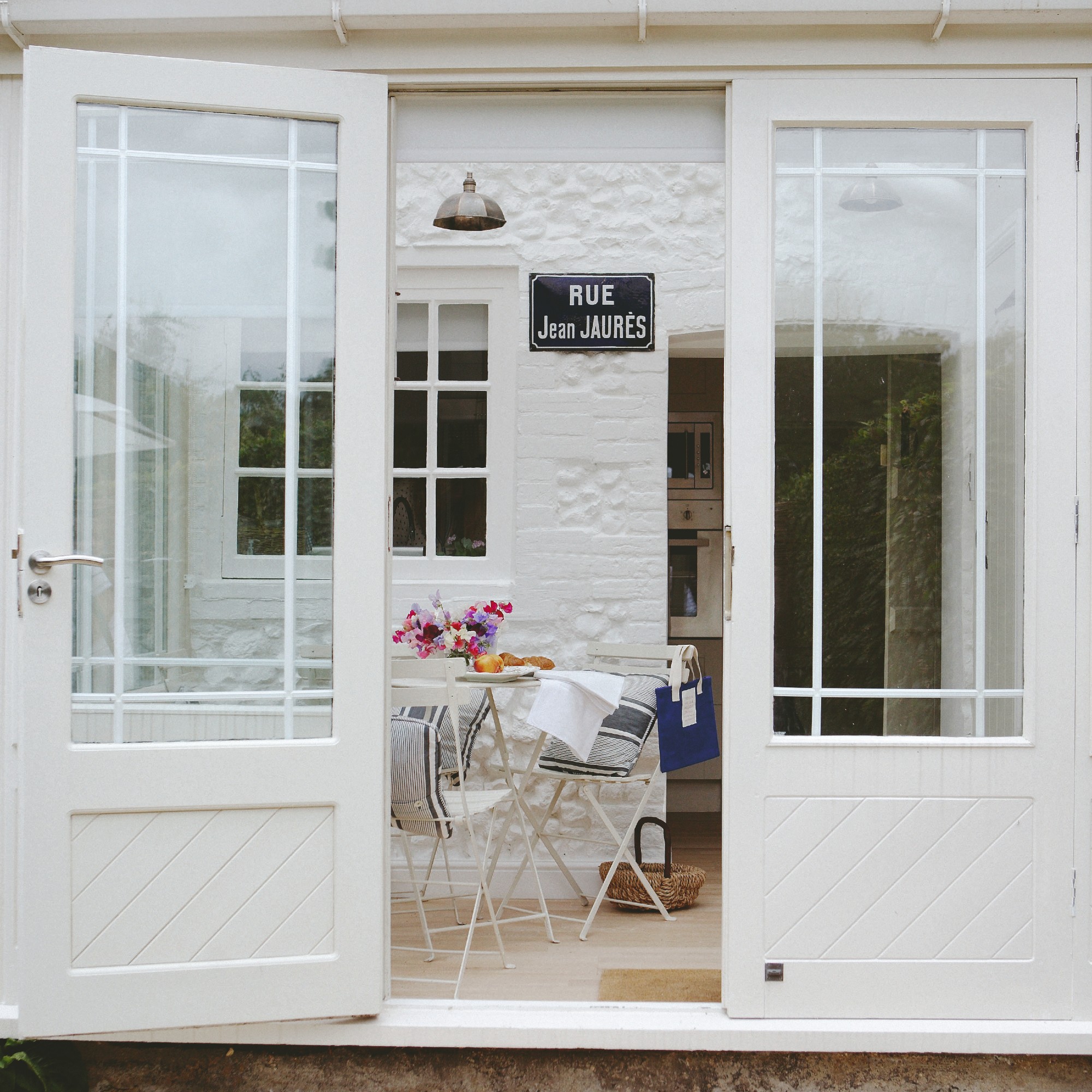 A small white conservatory with a white bistro set decorated with a vase of flowers and blue striped cushions