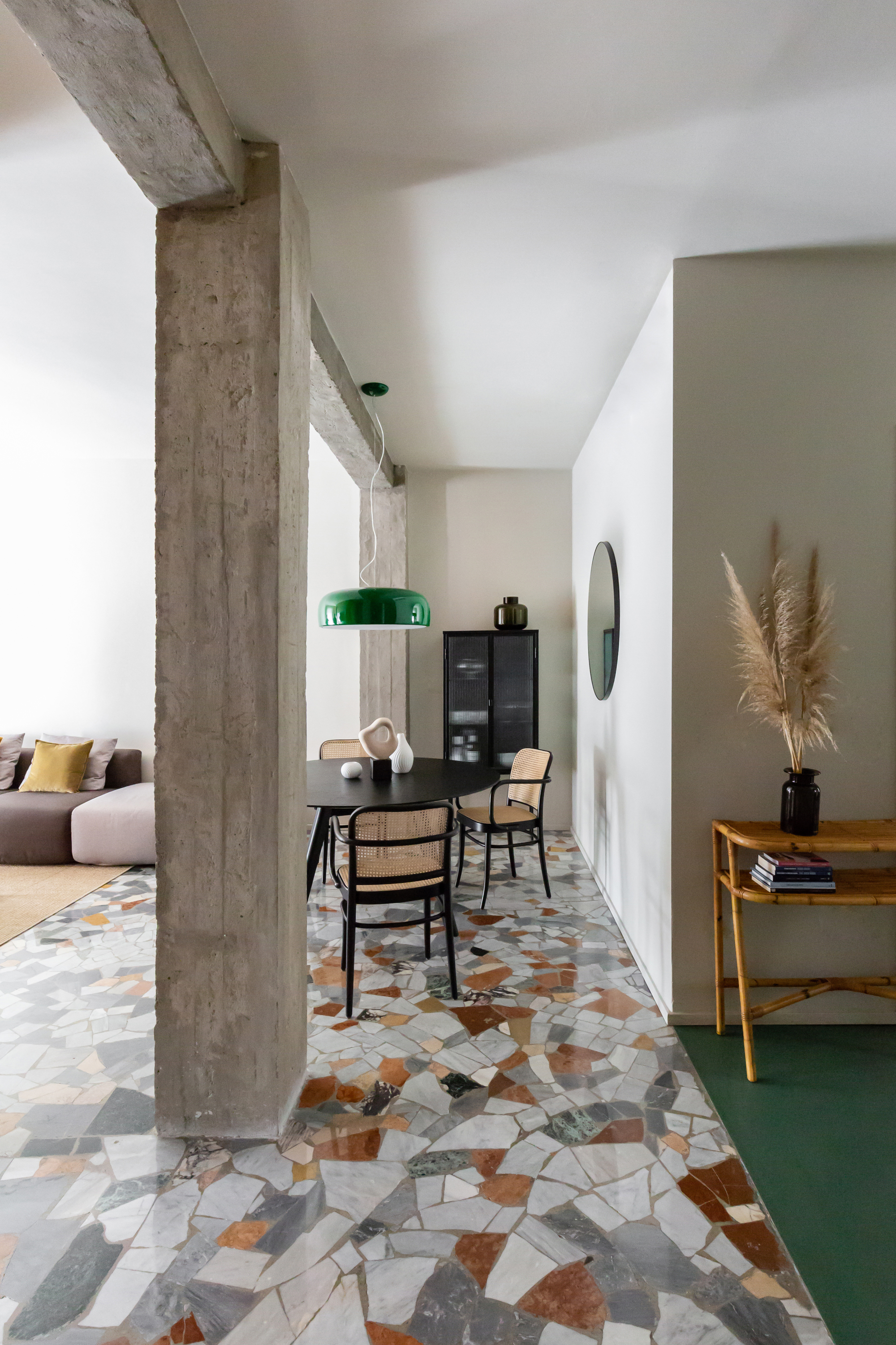 Image of an open concept living, dining, and entryway. The dining area has gray, white, and orange Palladiana terrazzo flooring. The walls and ceiling are white and there is an industrial beam in the center of the room.