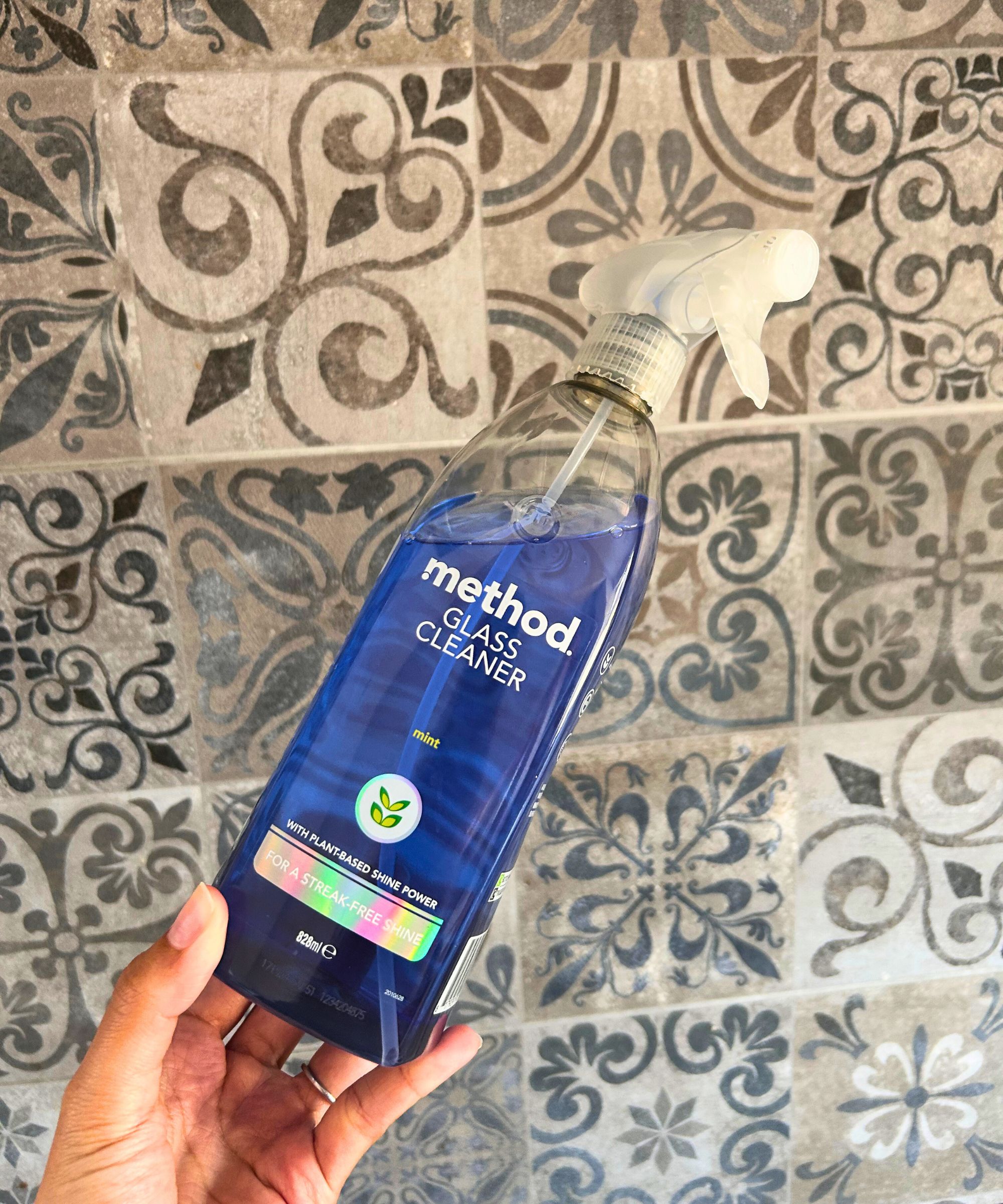 Person holding blue Method Glass cleaner in front of a tiled background