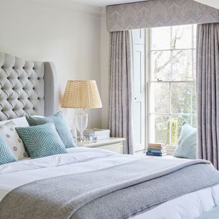 bedroom with grey curtains with pelment, cream walls and double bed with grey botton headboard and grey throw over white sheets