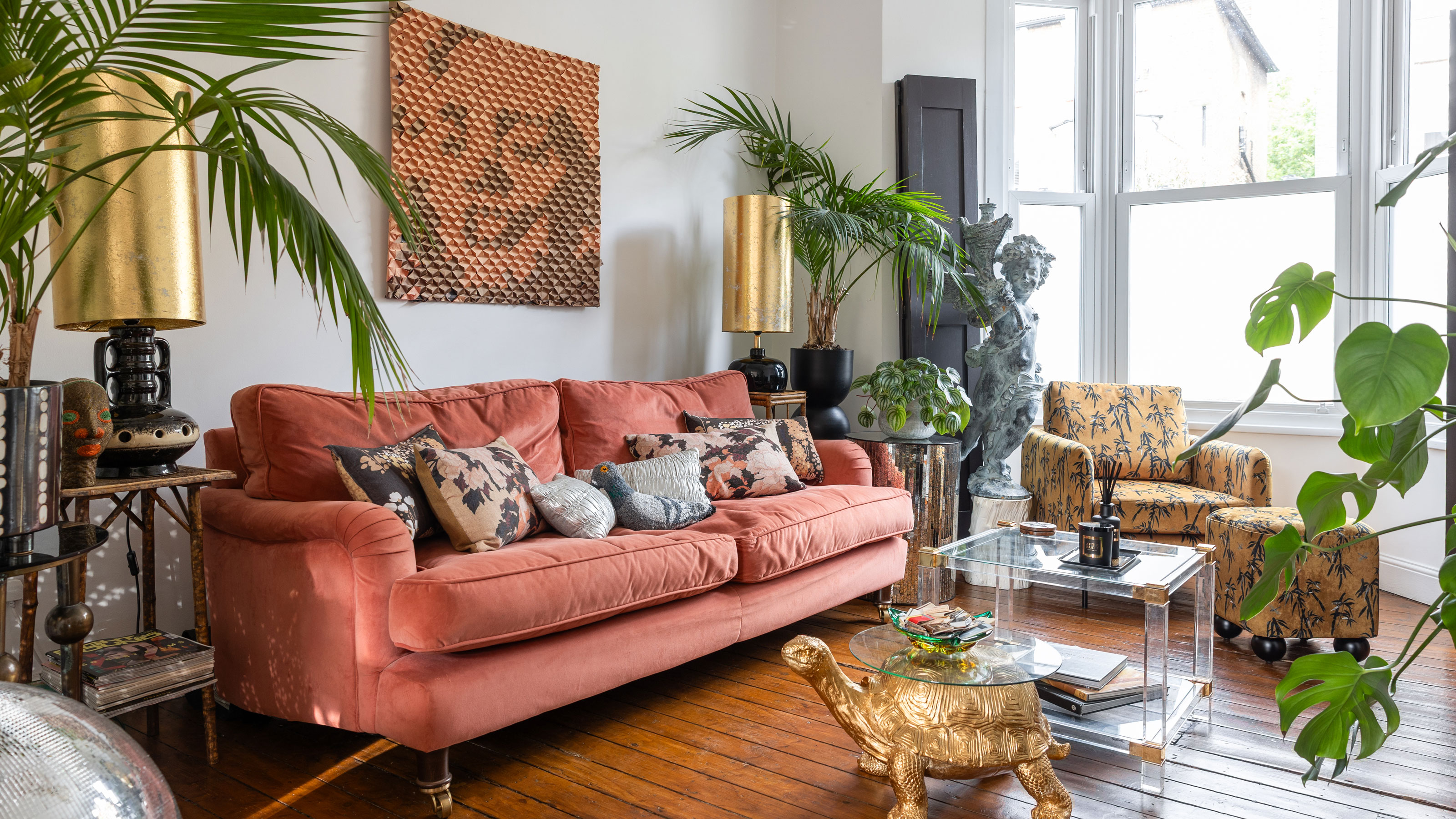 Pink sofa in white living room with gold table lamps, clear coffee table and gold armchair