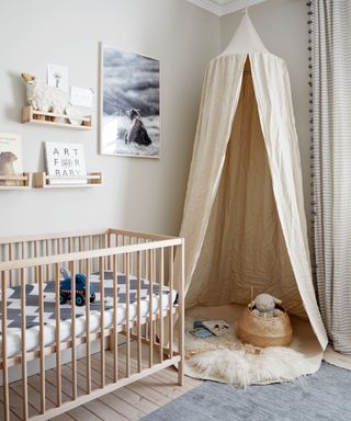Neutral nursery with hanging ceiling canopy, light wooden crib and shelving, grey rug