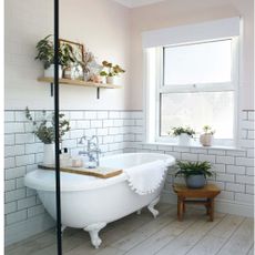 bathroom with white freestanding bath with wooden tray, wooden shelf with potted plants, wooden stool and white wall tiles