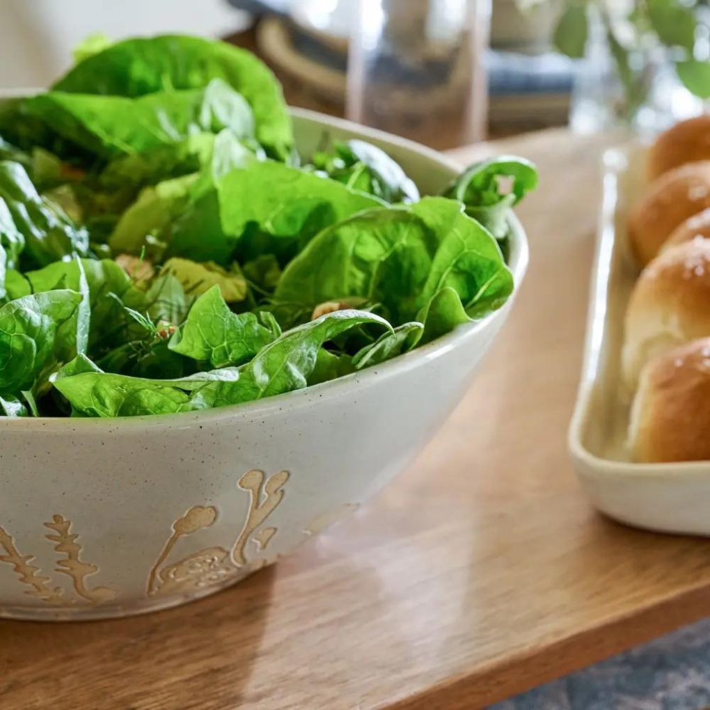 A serving bowl with gold flowers on the outside, filled with salad on a table