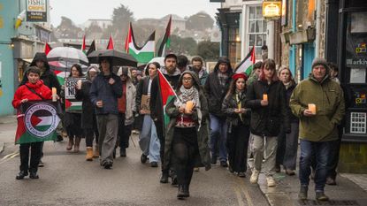 A group of people holding candles, Palestinian flags and signs