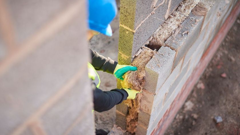 A builder in a blue hat installing insulation in a cavity wall void